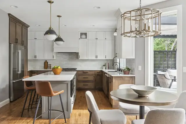 Open kitchen with white and stained wood cabinets, a gray island, brass pendants and a round dining table