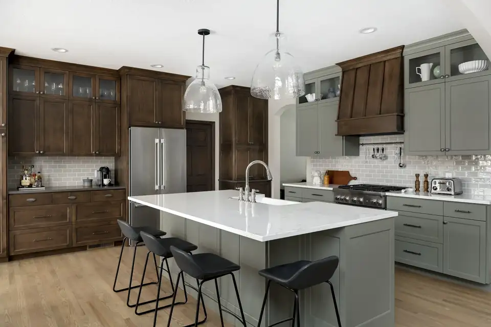 Lakeville kitchen with stained wood and sage green cabinets, a white island with black stools and glass pendants, by McDonald Remodeling, kitchen remodeler in Inver Grove Heights