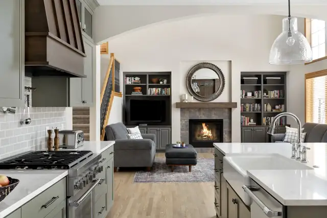 Lakeville kitchen with sage green cabinets and white counters opening to a family room with a fireplace and built-in shelves
