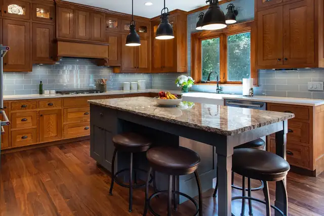Kitchen with quarter-sawn oak cabinets, a blue glass tile backsplash, a stone-topped island and black pendant lights