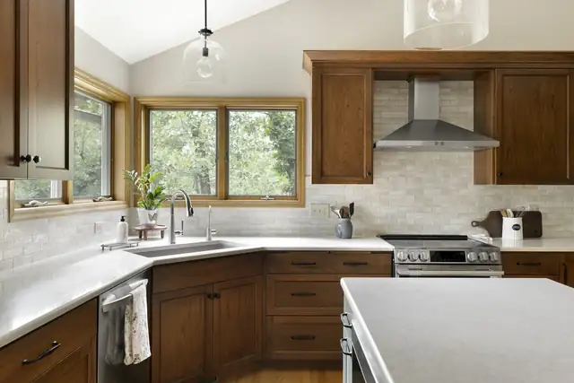 Kitchen with stained wood cabinets, white counters, a corner window over the sink and a stainless range hood
